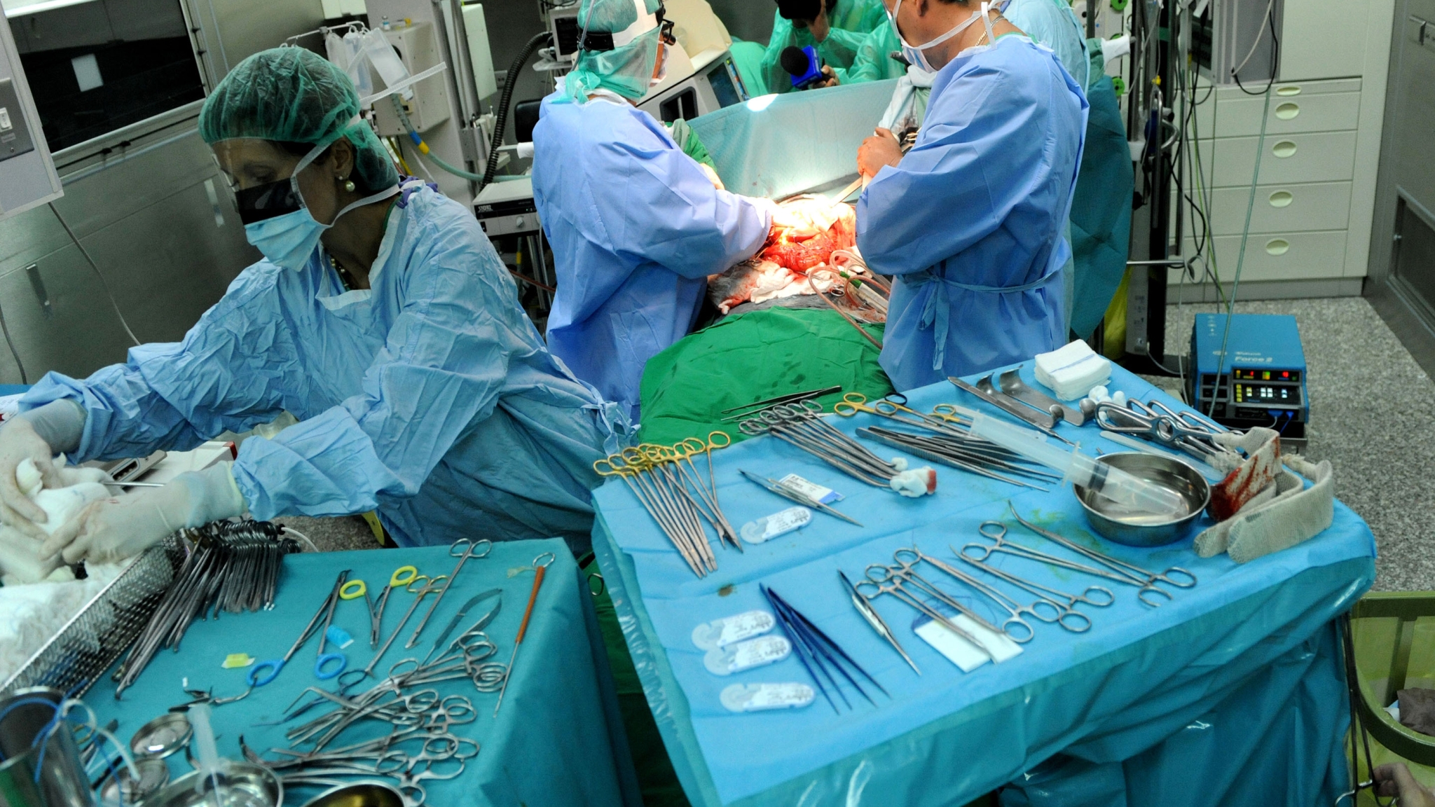 Surgeons in an operating room look at a patient while tools sit on a table