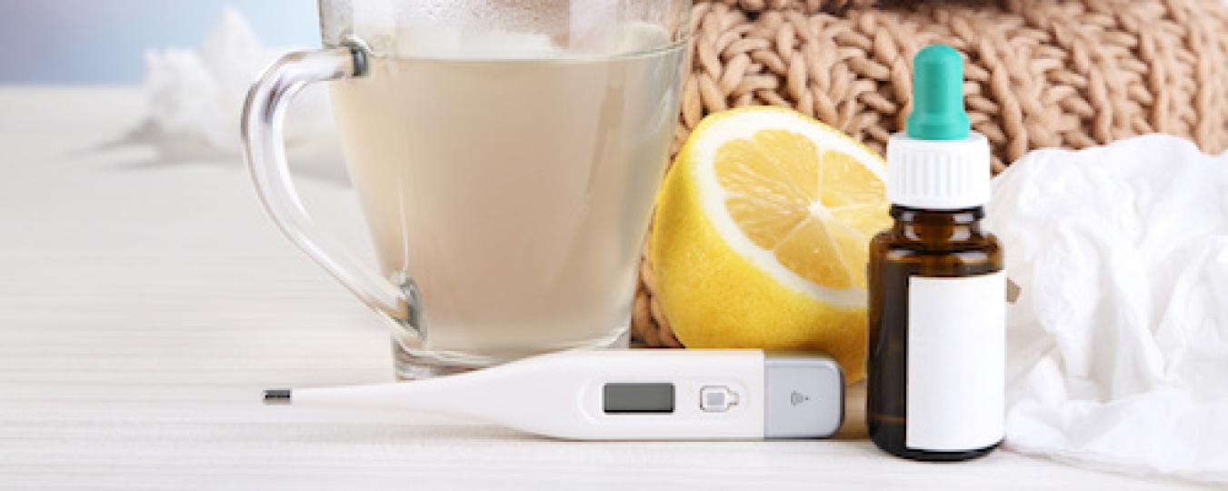 A cup of hot tea, a thermometer, a lemon and medicine