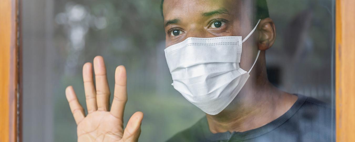 A man wearing a face mask looks out a window