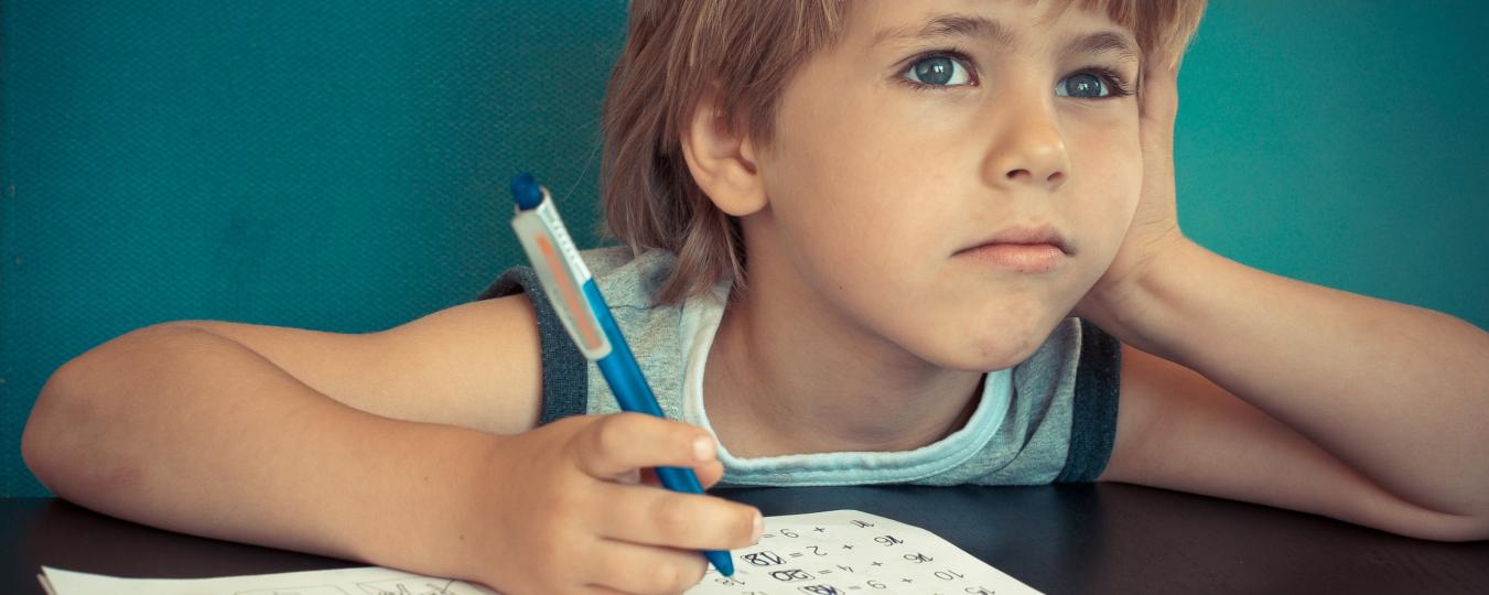 A child stares off as he does schoolwork