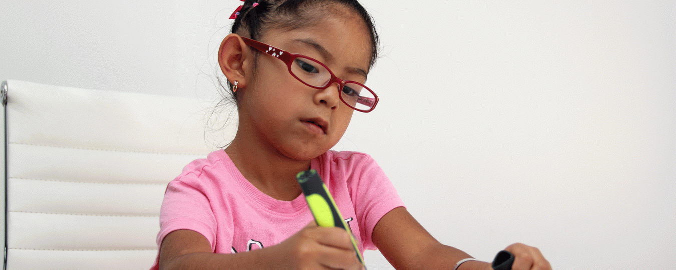 An autistic child wearing a pink shirt and glasses colors with a yellow marker