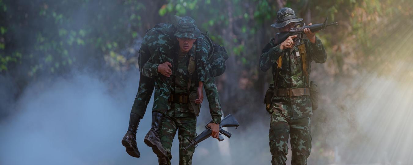 A soldier carries another who is injured in combat