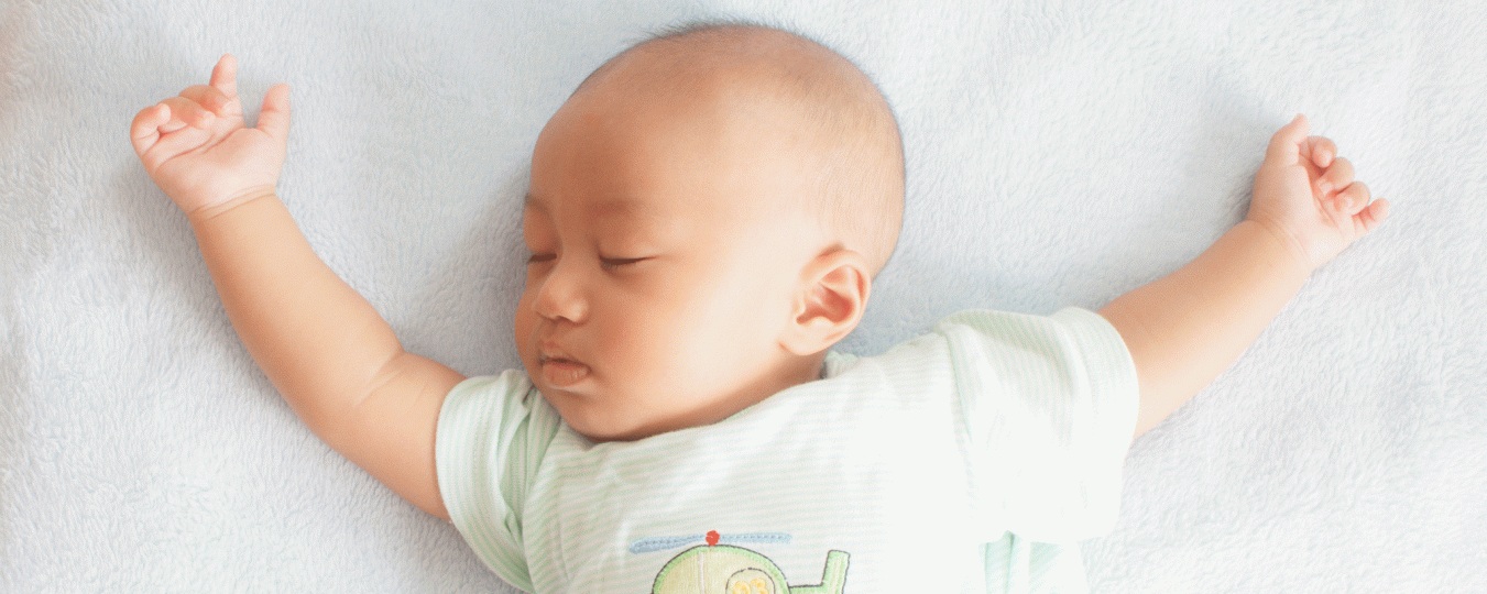 An newborn sleeps with arms outstretched on a blanket