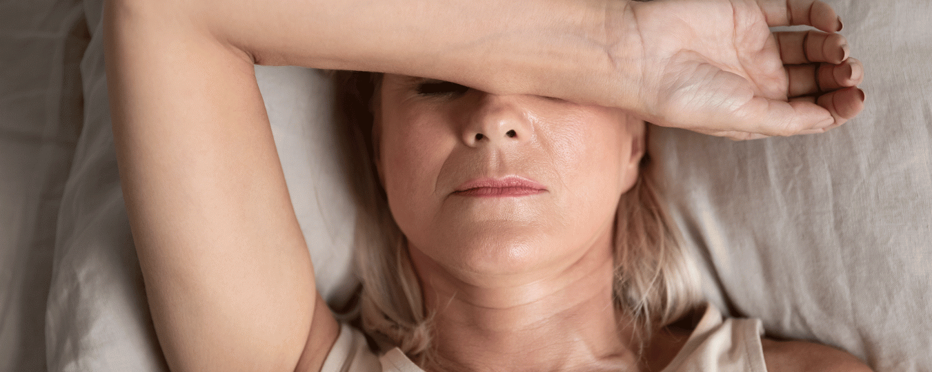 A woman covers her eyes with her arm while trying to sleep