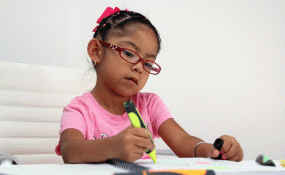 An autistic child wearing a pink shirt and glasses colors with a yellow marker