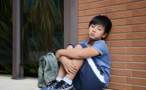 A child sits against a wall hugging his knees
