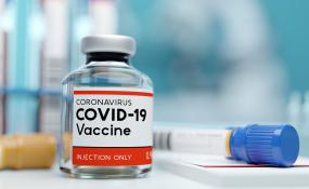 A covid-19 vaccine bottle sits on a table next to a syringe