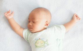 An newborn sleeps with arms outstretched on a blanket