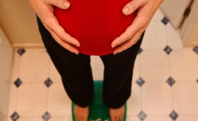 A pregnant woman cradles her bump while standing on a scale