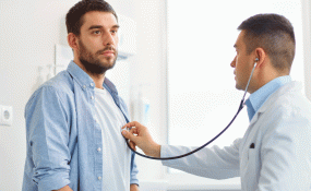 A doctor wearing a white coat uses a stethoscope to listen to a patient's heartbeat