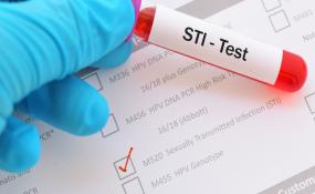 a blue gloved hand holds an STI test vial